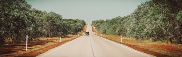 Geländewagen mit Anhänger fährt auf einsamer Straße durch Buschlandschaft in Westaustralien