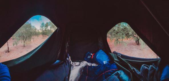 Blick aus dem Dachzelt auf den Busch bei Sonnenaufgang mit Schlafsack im Vordergrund