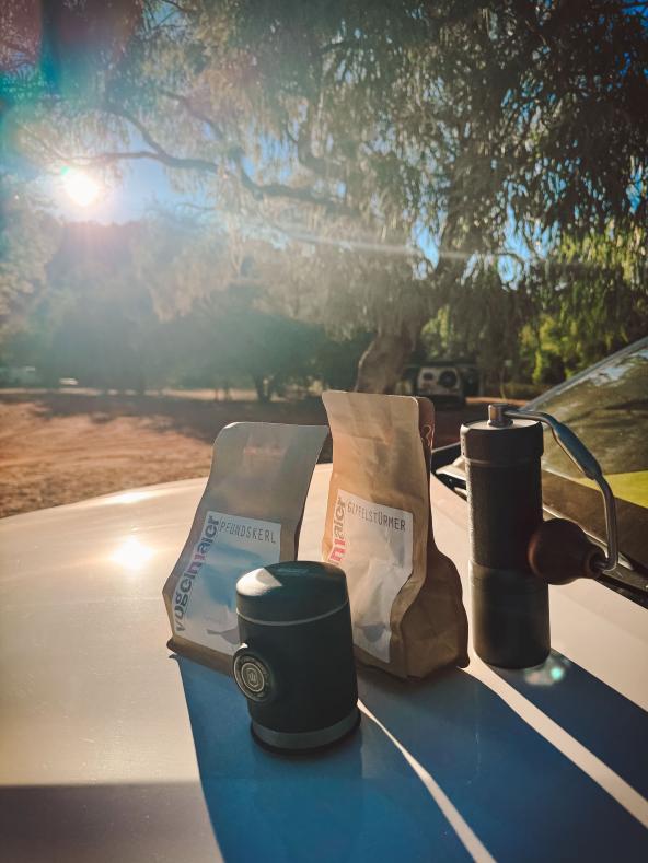 Kaffeebohnen und Handmühle auf Autodach im Morgenlicht im Outback