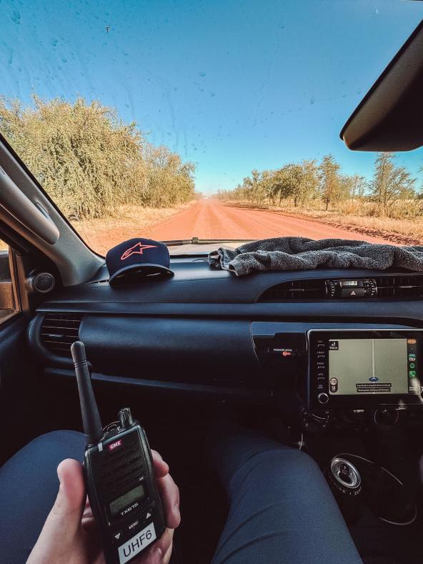 Blick aus einem Geländewagen auf eine rote Outback-Piste, Hand mit Funkgerät im Vordergrund