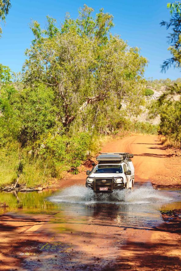 Geländewagen durchquert eine seichte Wasserstelle auf roter Schotterstraße