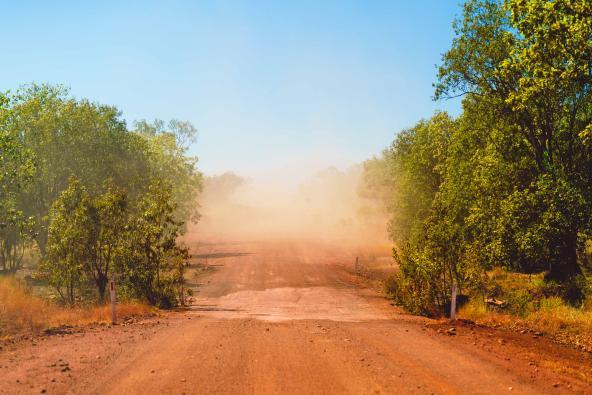 Staubige rote Schotterstraße im Outback mit aufgewirbeltem Sand in der Luft