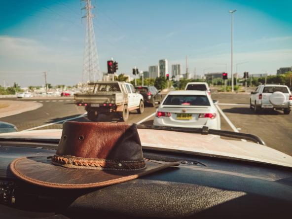 Lederhut auf staubiger Armatur, Blick durch die Frontscheibe auf Ampeln, Autos und wenige Hochhäuser.