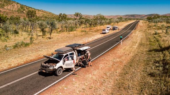 Reisende wechseln einen Reifen am Geländewagen auf einer einsamen Straße im australischen Outback.