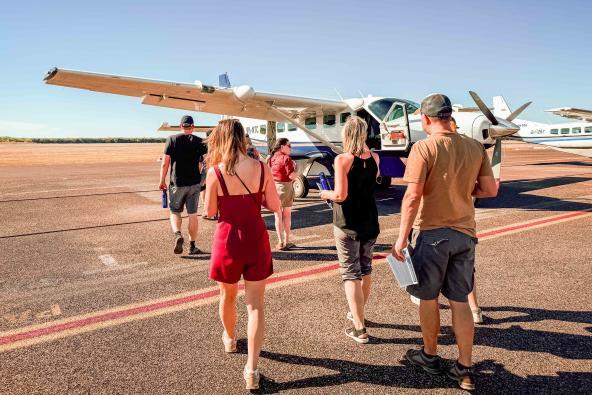 Reisende gehen über das Rollfeld zu einem kleinen Propellerflugzeug in Kununurra für einen Rundflug über die Bungle Bungle Range.