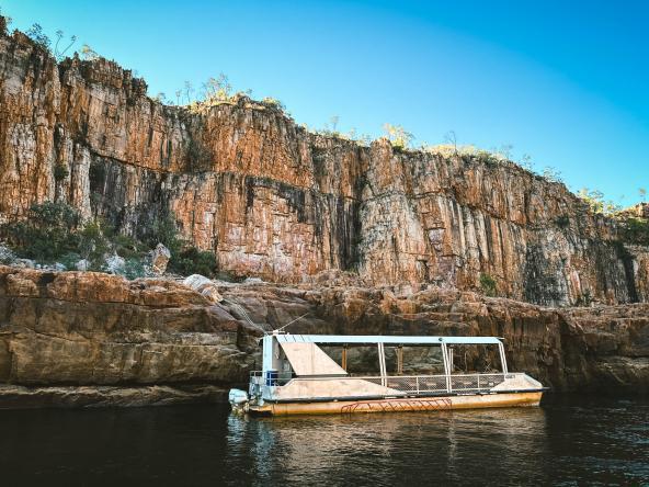Tourboot liegt im ruhigen Wasser der Katherine Gorge vor hohen, orangefarbenen Felswänden.