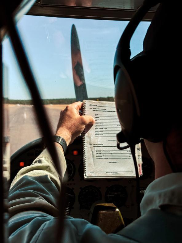 Pilot im Cockpit einer kleinen Propellermaschine, der eine Checkliste vor sich hält.